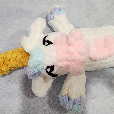 Peluche cavalo branco com crina rosa e azul sobre fundo cinzento