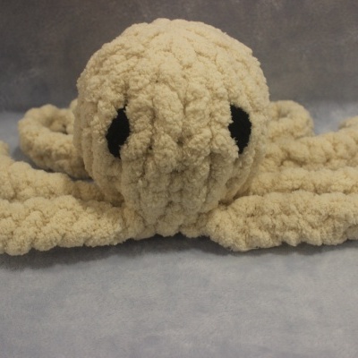 Polvo de peluche felpudo bege com olhos pretos sobre superfície azul