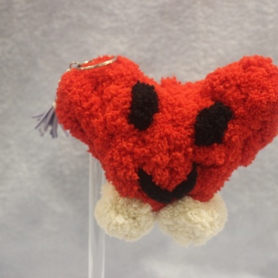 Chaveiro de coração de tecido felpudo vermelho com olhos e sorriso a preto e pompons brancos