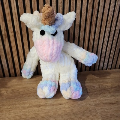 Pelúcia de unicórnio colorida em tons pastel sobre superfície de madeira