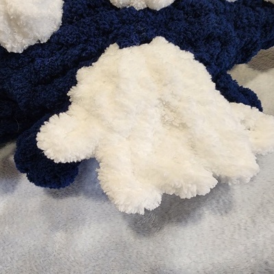 Pelúcia azul escura e branca, textura macia, sobre fundo cinzento.