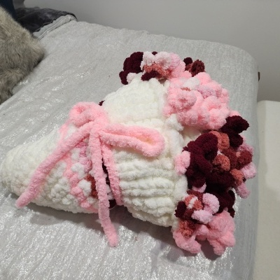 Bouquet de flores de lã coloridas sobre superfície prateada numa cama.