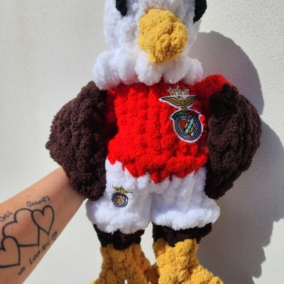 Pelúcia de águia branca com bico e patas amarelas, asas castanhas e roupa vermelha com emblema Benfica