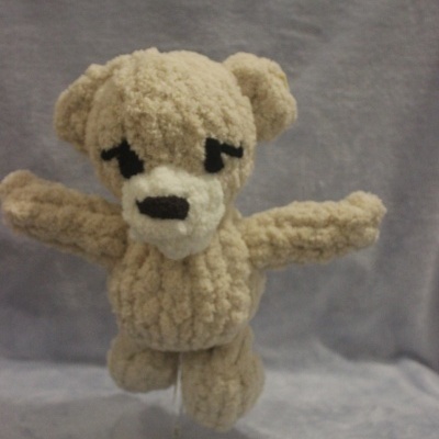 Peluche de urso bege com olhos e nariz preto num fundo cinzento