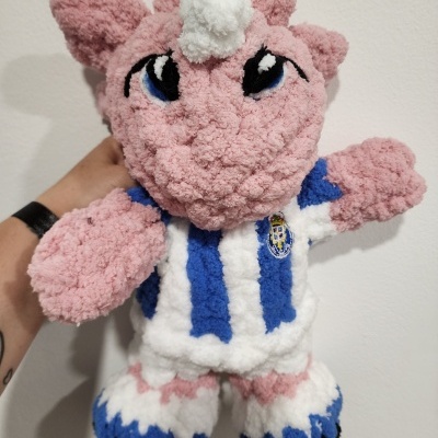 Pelúcia unicórnio cor-de-rosa com camisola azul e branca com emblema