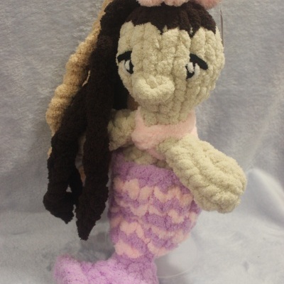 Boneca sirene tecido peludo creme com cauda lilás e rosa e laço rosa na cabeça
