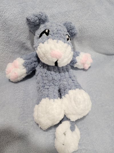 Peluche cinza e branco com detalhes rosa sobre tecido cinza claro