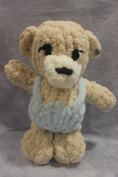 Ursinho de peluche bege com vestido azul claro em fundo cinzento