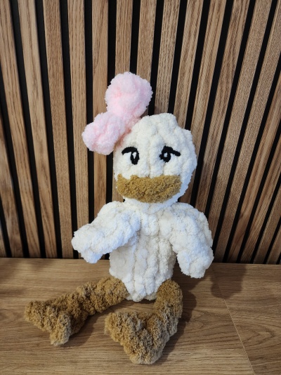 Boneco de pelúcia de pato branco com laço rosa sentado em superfície de madeira