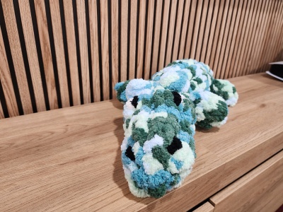 Pelúcia em forma de crocodilo com padrão azul, verde, branco e preto sobre superfície de madeira