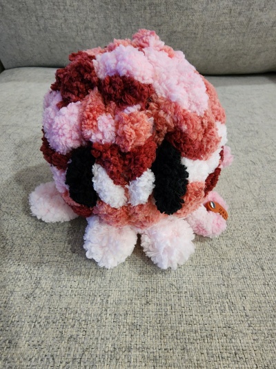 Pelúcia artesanal felpuda cor-de-rosa, vermelho, branco e preto com etiqueta de couro num sofá cinzento