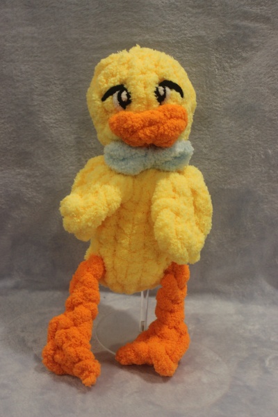 Peluche de pato amarelo com bico e pés laranja e laço azul claro