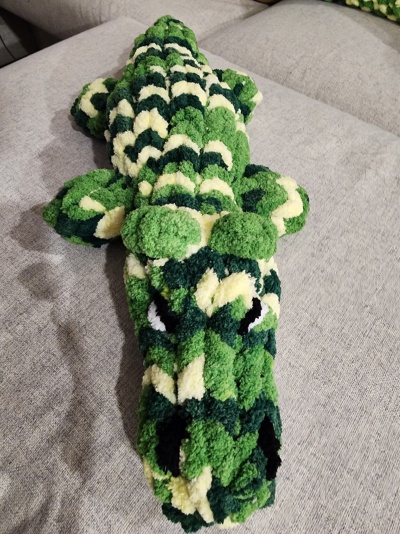 almofada felpuda em forma de crocodilo verde e branco numa superfície cinza