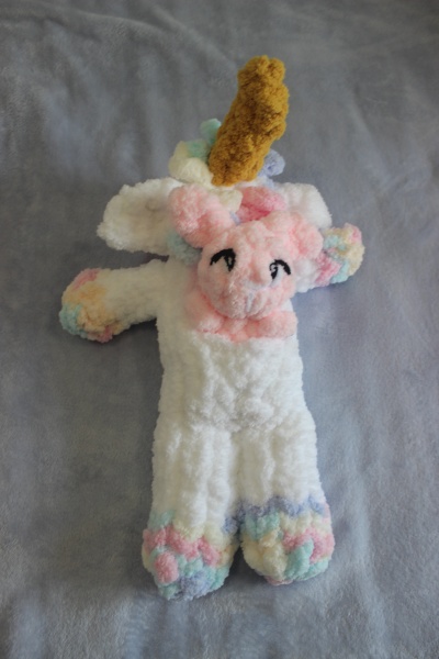 Pelúcia de unicórnio com corpo branco e detalhes coloridos sobre superfície cinzenta