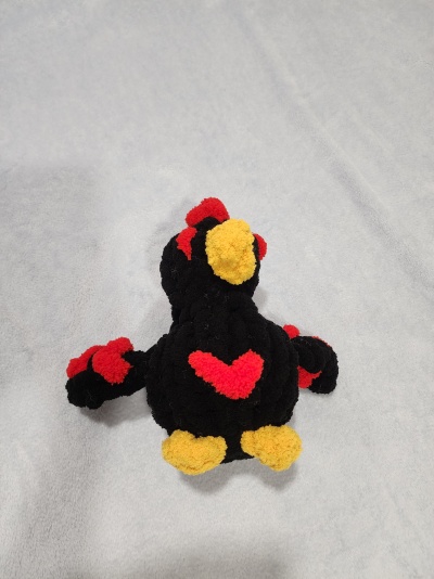 Pelúcia preta com detalhes vermelhos e amarelos sobre tecido cinzento claro