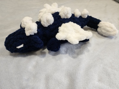 Pelúcia de dinossauro azul escuro com manchas brancas, texturas felpudas