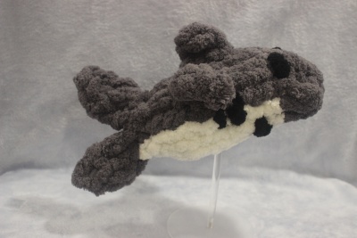 Pelúcia felpuda em forma de orca cinzenta e branca sobre suporte transparente