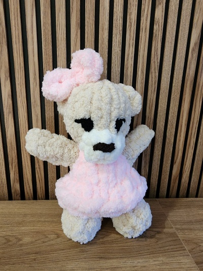 Urso de peluche castanho claro com vestido e laço rosa, olhos e nariz pretos