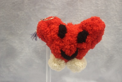 Chaveiro de coração de tecido felpudo vermelho com olhos e sorriso a preto e pompons brancos