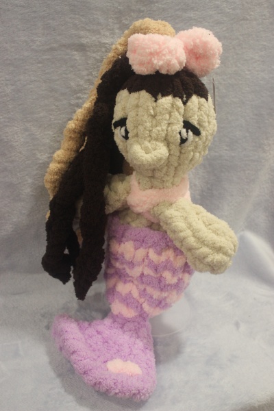 Boneca sirene tecido peludo creme com cauda lilás e rosa e laço rosa na cabeça