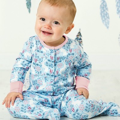 Bebé sentado com macacão azul estampado com coelhinhos e vegetação e punhos rosa claros