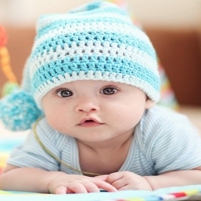 Bebé com chapéu de crochet azul e branco deitado sobre tapete colorido