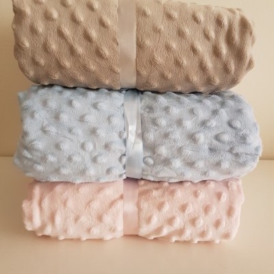 Três mantas felpudas empilhadas em bege, azul claro e rosa com padrão de bolinhas