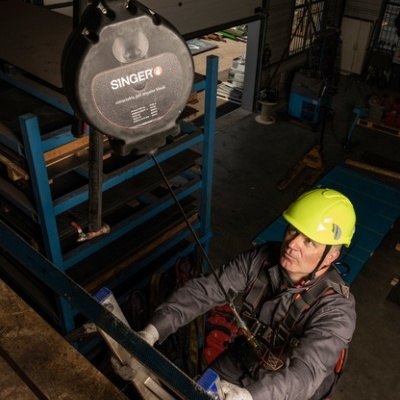 Dispositivo de segurança SINGER Safety suspenso e trabalhador com capacete amarelo e roupas de proteção em ambiente industrial