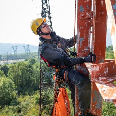 Trabalhador com equipamento de segurança a escalar estrutura metálica laranja