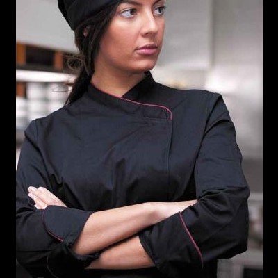 Mulher com casaco de chef preto e gorro preto numa cozinha profissional