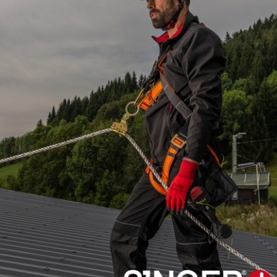 Homem com equipamento de segurança e capacete em telhado metálico cinzento, com vegetação ao fundo