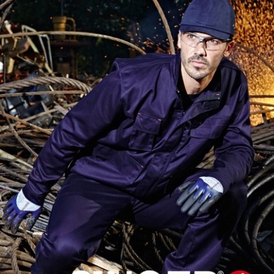 Homem em fato macaco azul escuro com luvas e boné num ambiente industrial com faíscas