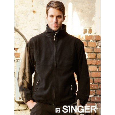 Homem com casaco preto com fecho e bolsos, parede de tijolos vermelhos e branca ao fundo