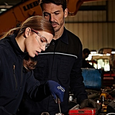 Duas pessoas com roupa de trabalho preta e óculos de proteção numa oficina