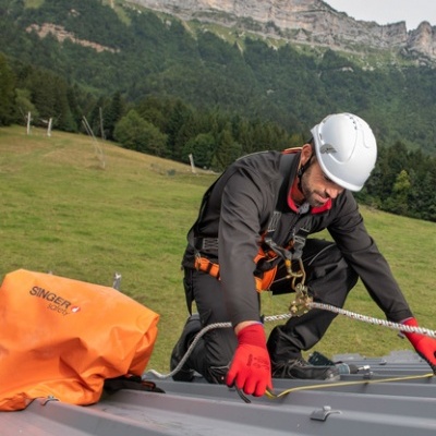 Homem com equipamento de segurança a trabalhar numa estrutura metálica com mochila laranja SINGER ao ar livre em montanha