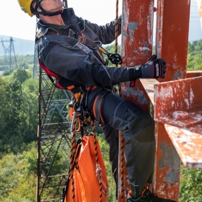Trabalhador em equipamento de segurança a escalar estrutura metálica oxidada com vegetação ao fundo