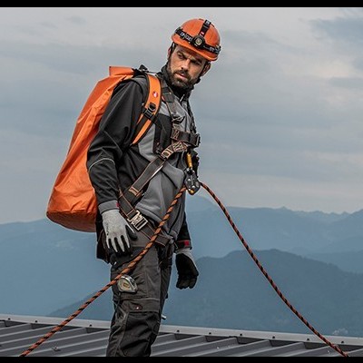 Homem com capacete de segurança e arnês em cobertura metálica com montanhas ao fundo