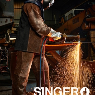 Trabalhador industrial com equipamento de protecção e ferramenta a produzir faíscas numa oficina, texto 'SINGER safety'