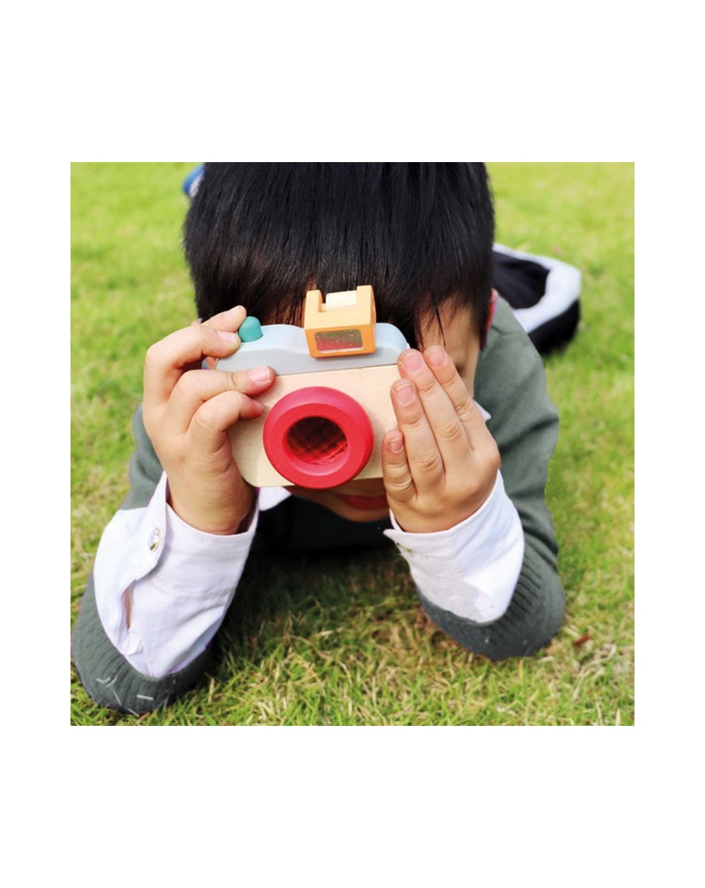 Máquina Fotográfica de Madeira Criança deitada na relva a brincar com câmara de brinquedo de madeira colorida