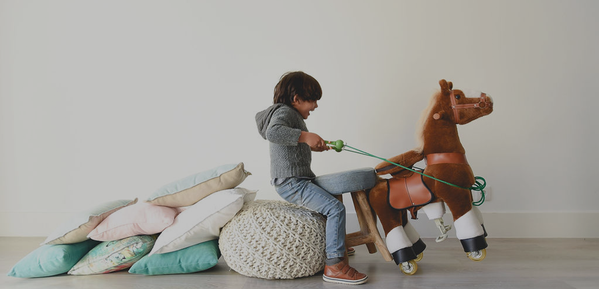Criança a brincar com cavalo de brinquedo em ambiente interior com almofadas e pufe