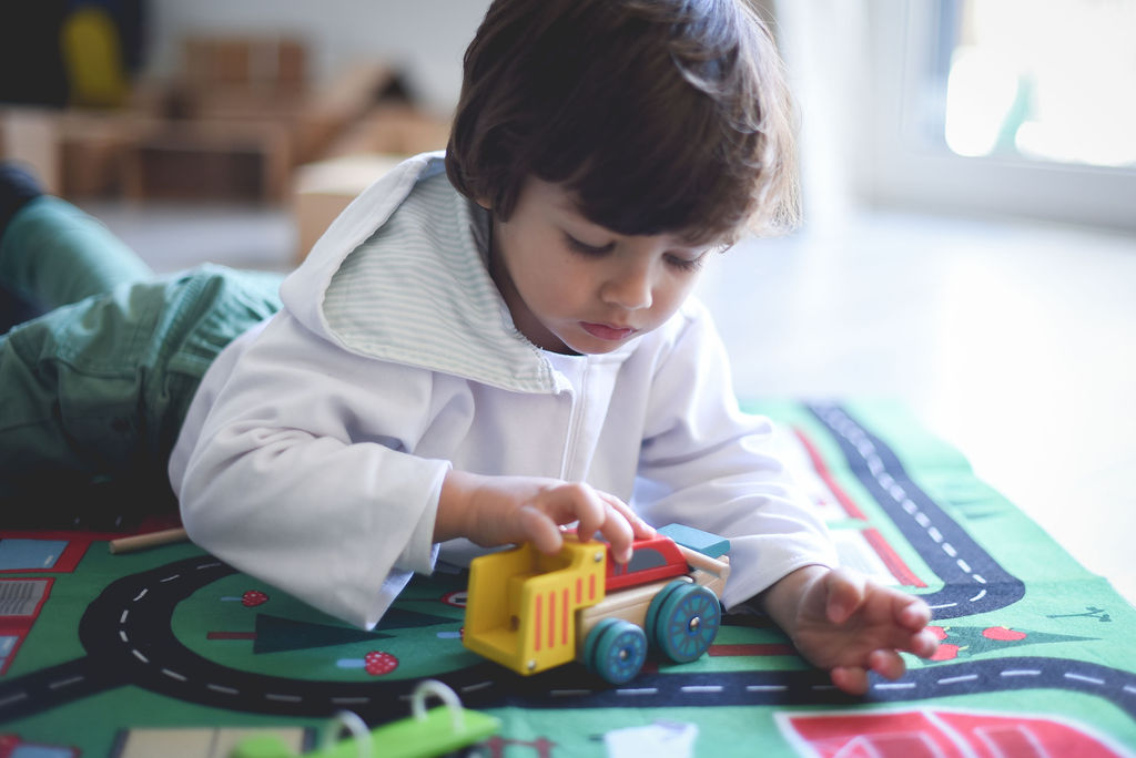 Menino a brincar com carrinho de madeira numa alcatifa com estradas.