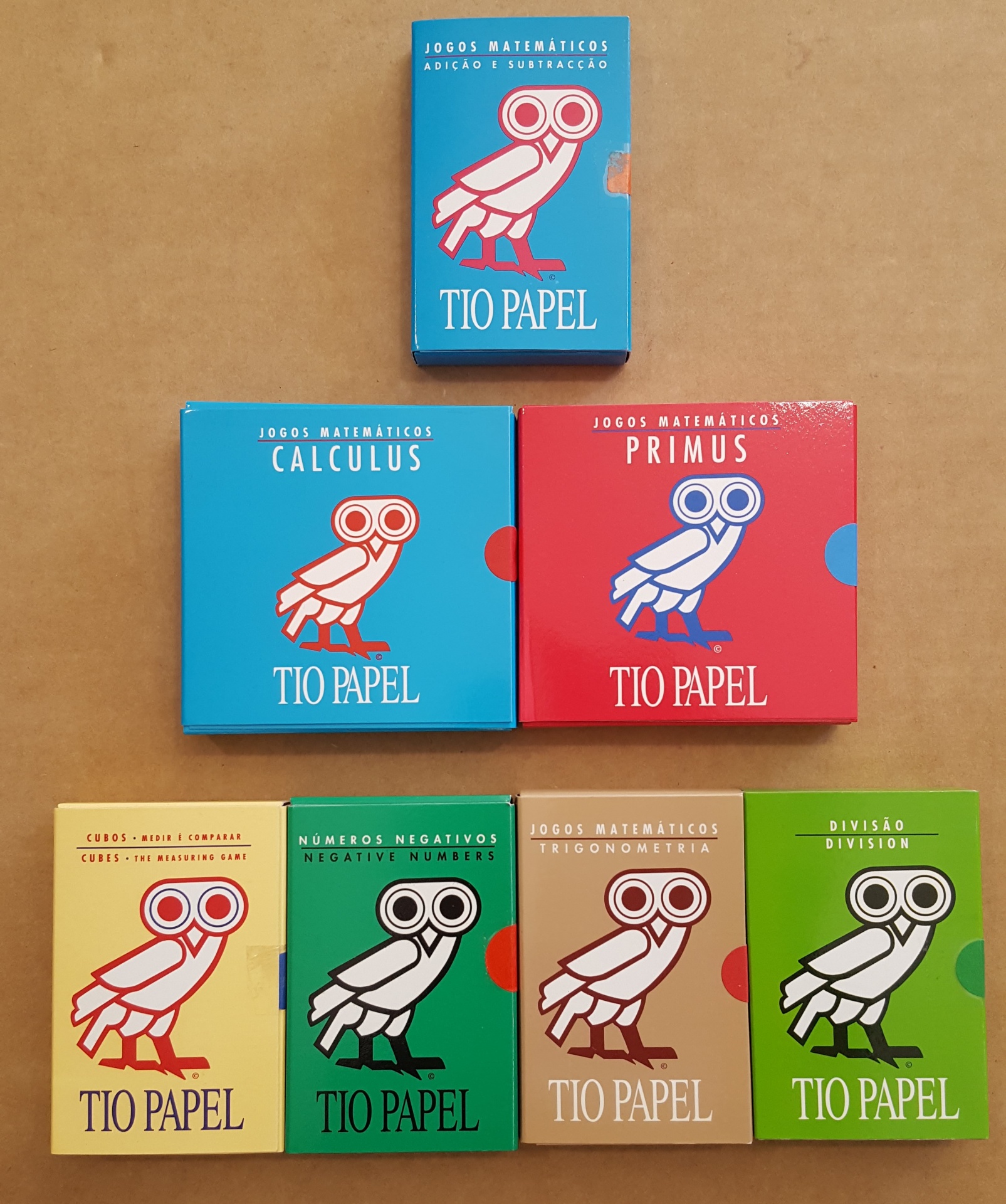Caixas coloridas de jogos matemáticos TIO PAPEL com logotipo de coruja em fundo castanho.