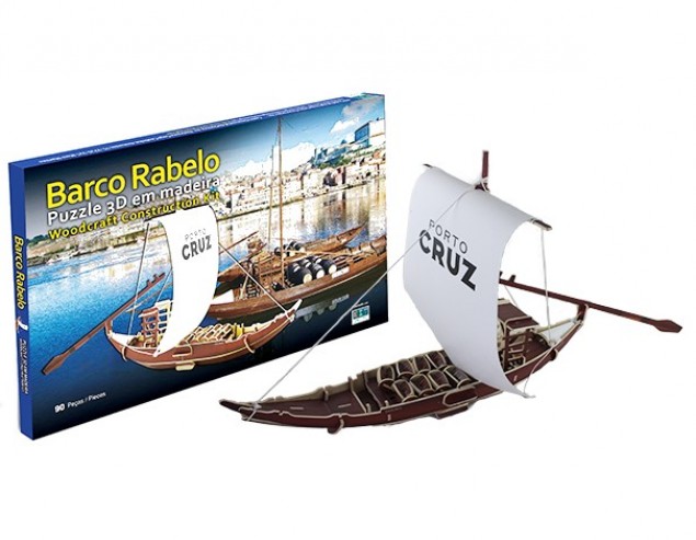 Barco Rebelo Puzzle 3D em madeira do Barco Rabelo com vela branca e remos ao lado da caixa do produto
