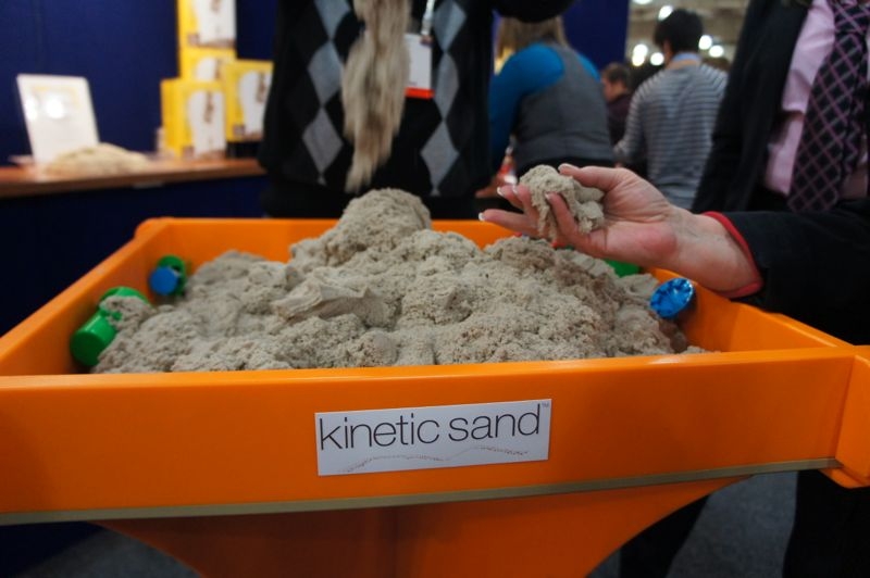 Areia Cinética (5kg) Balde laranja com areia cinzenta 'kinetic sand' e mão a moldar areia em evento