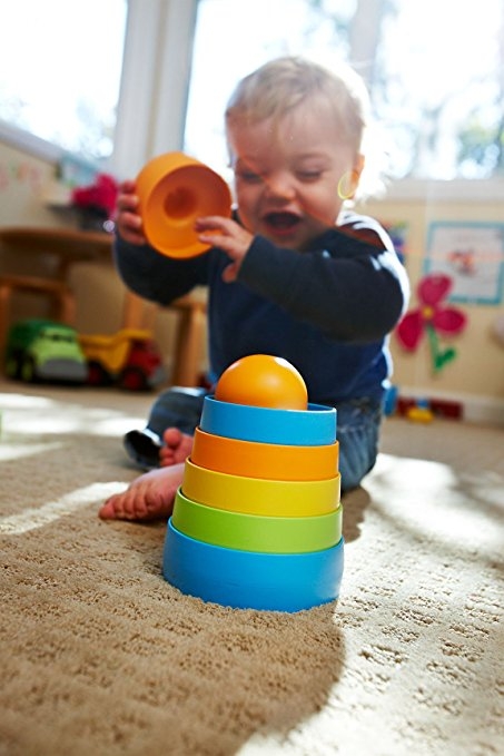 Criança brinca com copos empilháveis coloridos em tapete num quarto iluminado
