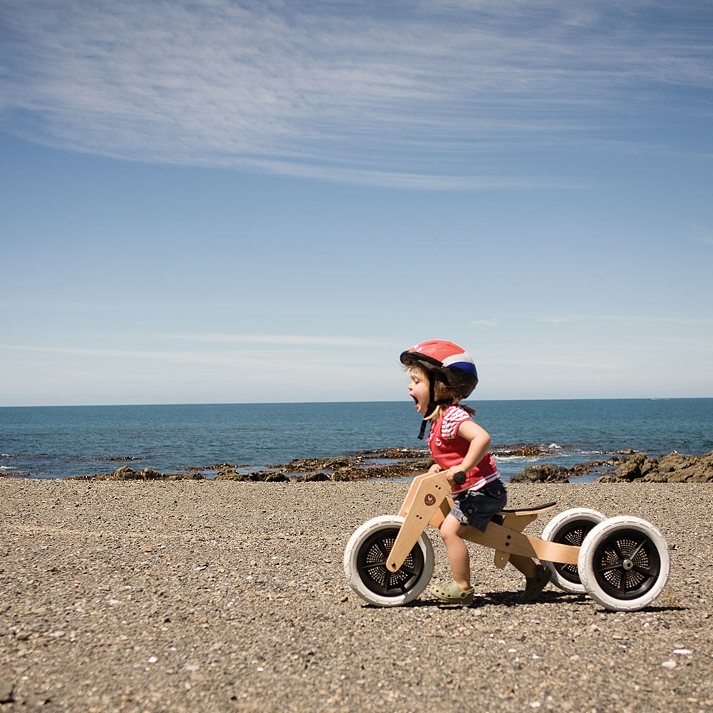 Criança com bicicleta de equilíbrio de madeira na praia