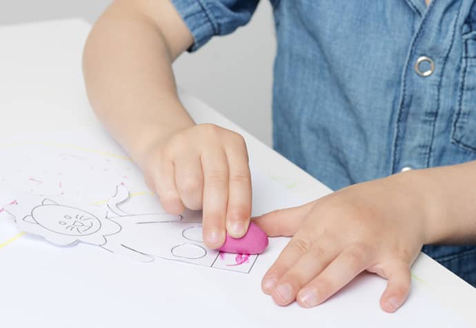 Crayon Rocks - Saco algodão (32) Criança a apagar desenho num papel com borracha rosa na mesa branca