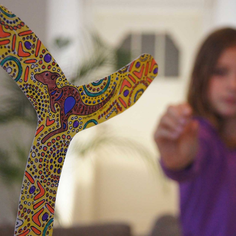 Boomerang - My Fibo Estilingue colorido em madeira com padrões abstratos e criança ao fundo