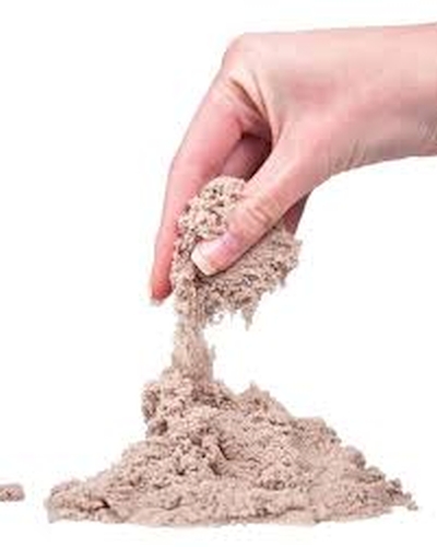 Areia Cinética (5kg) Mão segurando areia fina cinzenta sobre uma superfície com mais areia.