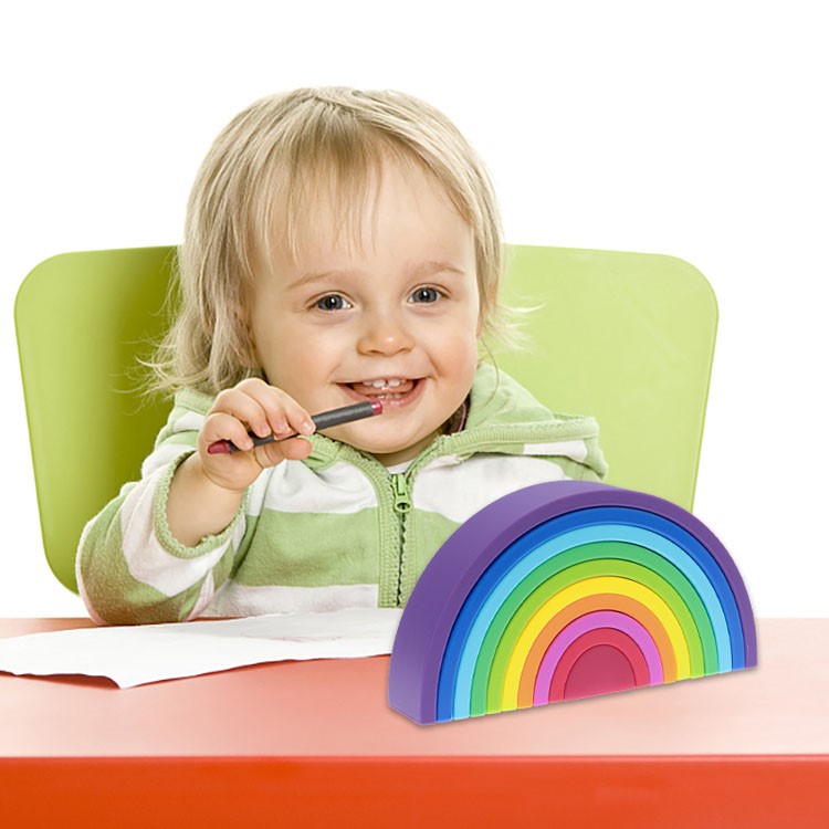 Arco Iris 10 Pcs Criança sorridente com casaco verde e branco sentada numa mesa com brinquedo arco-íris colorido